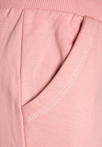 Lichtroze stof met een gladde textuur heeft een zijzak en een geribde tailleband. Stikdetails zijn zichtbaar.
