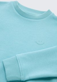 Light blue sweatshirt with a ribbed neckline and cuffs, featuring a subtle embroidered smiley face on the front. Soft fabric texture.