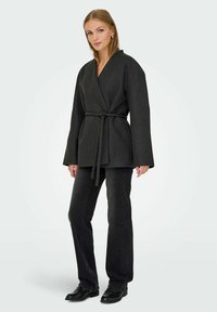 Dunkelgraue Wickeljacke aus Wollmischung mit weiten Ärmeln und einem Bindegürtel in der Taille. Kombiniert mit schwarzen geraden Jeans und Schuhen.
