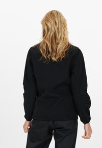 Svart jacka med långa ärmar, veckade manschetter och en slät yta. Har en minimalistisk design och lätt formning vid axlarna.