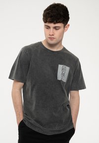 Dark gray cotton t-shirt featuring a front pocket with a white graphic design. The shirt has a relaxed fit and crew neck design.