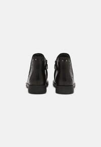 Botas de cuero negras hasta el tobillo con un acabado suave, con tachuelas metálicas a lo largo de los lados, punta redondeada y un tacón bajo de goma.