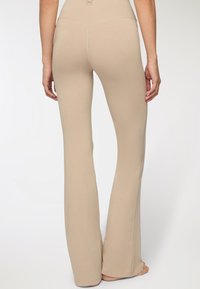 Beżowe, rozszerzane spodnie do jogi z elastycznego materiału, posiadające wysoki stan i wzmocnione szwy po bokach. Gładka faktura.