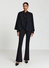 Blazer nero su misura con maniche a campana, abbinato a pantaloni neri a vita alta. L'outfit presenta un foulard al collo e scarpe nere a punta.