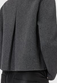 Blazer en laine gris avec une finition texturée, doté d'un détail de pli à l'arrière, d'épaules structurées et d'une silhouette courte.