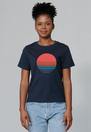 T-shirt en coton bleu marine avec un motif circulaire d'un soleil rouge et des lignes horizontales colorées en bleu, orange et vert en dessous.