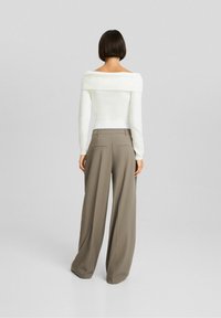 Suéter de punto blanco con escote off-the-shoulder y textura acanalada, combinado con pantalones sueltos beige que presentan bolsillos traseros y un diseño a medida.