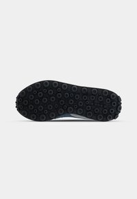 Black rubber outsole with circular tread pattern, showcasing texture contrast against a light blue midsole for grip and support.
