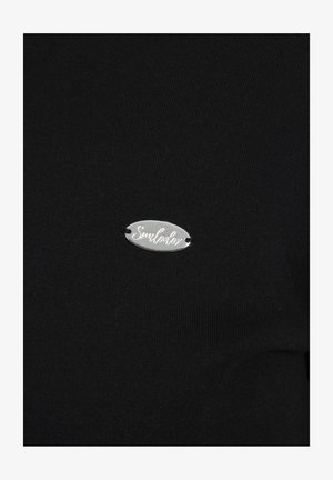 Schwarzes Stretch-Top aus Stoff mit einem kleinen silbernen ovalen Anhänger, auf dem "Simulador" in Kursivschrift eingraviert ist. Die Textur wirkt glatt und enganliegend.