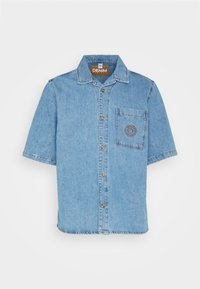 Gaiša zila īsām piedurknēm džinsa krekls ar krūšu kabatu, kurā ir izšūts apļveida raksts un brūni pogas.