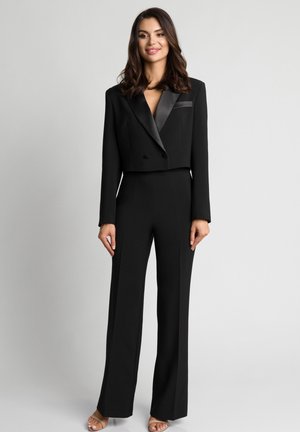 Czarna krótka marynarka z satynowymi klapami i pasujące szerokie spodnie. Gładka tkanina, dopasowany krój i głęboki dekolt w serek. Wyraźne linie kroju.