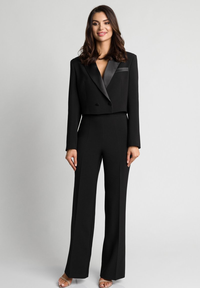 Czarna krótka marynarka z satynowymi klapami i pasujące szerokie spodnie. Gładka tkanina, dopasowany krój i głęboki dekolt w serek. Wyraźne linie kroju.