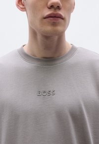 Világosszürke pulóver puha anyagból. Kerek nyakkivágással és egy finoman dombornyomott "BOSS" logóval a mellkason. Sima textúrájú és laza szabású.