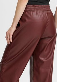 Bordeaux kleurige nepleer broek met een relaxte pasvorm, voorzien van een elastische tailleband en een gladde textuur, met een licht glanzende afwerking.