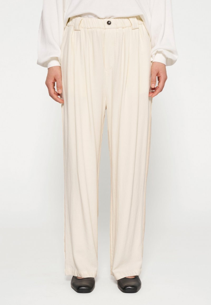 Crème kleurige broek met een relaxte pasvorm, voorzien van een geplooide tailleband en een enkele knopdetail. Soepele stof met een subtiele glans.