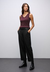 Bordeaux ærmeløs top parret med højtaljede sorte ternede bukser. Mat sorte ankelstøvler fuldender outfittet. Glat stoftekstur er tydelig.