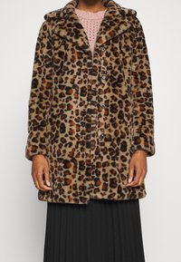 Leopardmönstrad fuskpälsjacka med en mjuk textur, stor krage, knappstängning och knälång design, bärs över en rosa stickad topp.