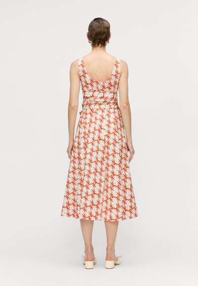 Eng anliegendes, ärmelloses Kleid mit tiefem Rückenausschnitt, weißem Stoff mit rotem Palmenblattmuster und einem ausgestellten, knielangen Rock.