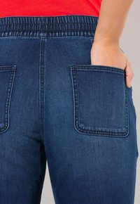 Mörkblå denimjeans med en figursydd midja, med två stora bakfickor och en slät textur.