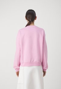 Růžový svetr s kulatým výstřihem, dlouhými rukávy a žebrovanými manžetami. Měkká textilie s volným střihem, kombinovaný s bílou sukní.