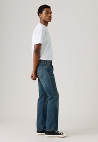 Light blue t-shirt paired with dark blue straight-leg jeans and black sneakers. The jeans feature a classic five-pocket design.