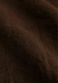 Gros plan sur un tissu texturé brun foncé avec un tissage visible et des plis doux créant de légères ombres.