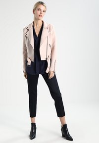 Roza suede moto jakna s patentima, nošena preko mornarsko plave bluze, u kombinaciji s teksturiranim crnim hlačama do gležnjeva i crnim čizmama na visoku petu.