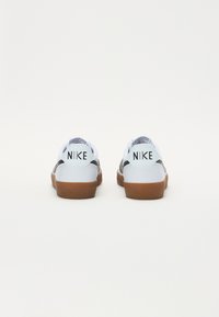 Nike sporta apavi ar baltu ādas virsotni, melniem akcentiem un brūnu gumijas zoli. Iezīmējas ar teksturētu aizmuguri un izteiktu logo detaļu.