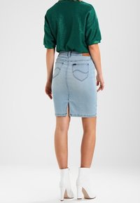 Ljust blå denimpencilkjol med en slits bak, kompletterad med hög midja och två bakfickor. Bärs med en grön topp och vita klackar.