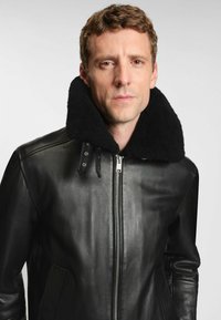 Schwarze Lederjacke mit einem samtigen schwarzen Schaffellkragen, Reißverschluss vorne, Seitentaschen und glatter Textur. Einfaches Design und taillierte Silhouette.