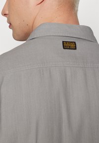 Grå skjorta med krage, försedd med ett G-Star Originals-märke på ryggen. Tillverkad av slät, vävd tyg med en subtil textur.