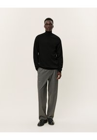Schwarzer Rollkragenpullover kombiniert mit grauen karierten Hose und schwarzen Schnürschuhen, mit langen Ärmeln und entspannter Passform.