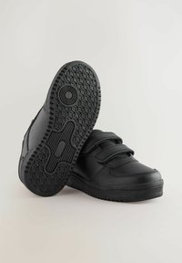 Schwarze Lederschuhe mit einer glatten Textur, ausgestattet mit doppelten Klettverschlüssen und einer gemusterten Gummisohle mit hexagonalen Profilen.