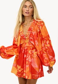 Robe florale rouge vif et orange avec des manches bouffantes, un décolleté en V profond, et une texture froncée autour du buste et de la taille.