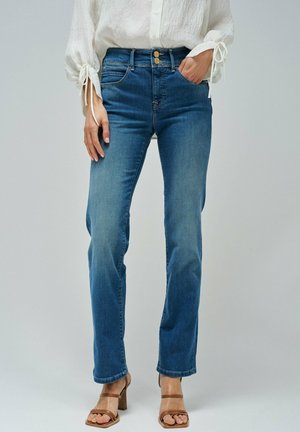 Jeans de denim azul claro con un diseño de pierna recta, dos bolsillos frontales y un cierre de botón, combinados con tacones beige de tiras.