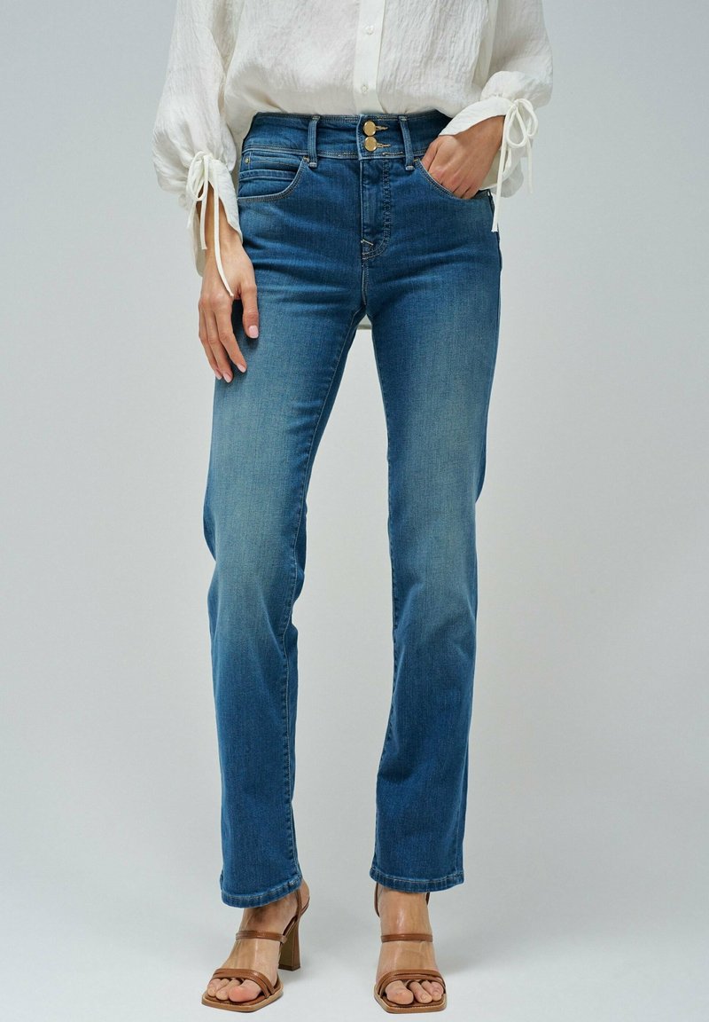 Jean en denim bleu clair avec une coupe droite, deux poches avant et une fermeture à bouton, associés à des escarpins beiges à brides.