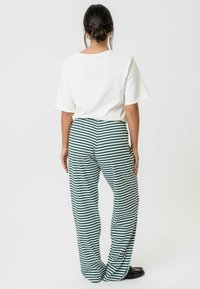 Bijela majica kratkih rukava u kombinaciji s hlačama širokog kroja u zeleno-bijelim prugama, s opuštenim krojem i mekim materijalom.