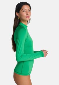 Traje de baño verde de manga larga con cuello alto, textura suave, diseño ajustado y costuras contrastantes, que exhibe un estilo minimalista.