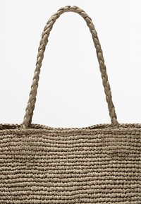 Geweven rieten tote bag in een lichte beige kleur, met een gevlochten handvat en een gestructureerd lichaam met een open bovenkant.