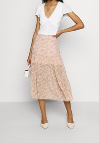 Haut blanc court à manches courtes et avec des boutons, assorti à une jupe midi fluide arborant un motif floral pastel. Des escarpins beiges à bout pointu complètent le look.