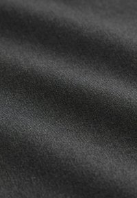 Gros plan d'un tissu lisse gris foncé avec un tissage fin et serré, présentant des plis subtils créant de douces ombres et une texture délicate.