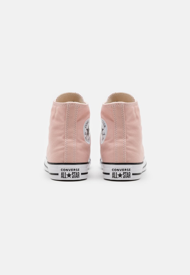 Zapatillas altas de lona rosas con suela de goma negra y blanca. Presentan un parche de logo circular en el lado exterior y costuras blancas.