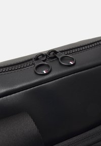 Borsa sintetica nera caratterizzata da una texture liscia, doppi zip neri con tiranti rotondi e un sottile dettaglio del logo in rosso, bianco e blu.