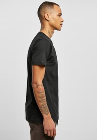 Sort bomulds T-shirt med korte ærmer og rund hals. Pasformen er afslappet, med synlige tatoveringer på armen.