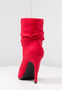 Botines de ante rojo con un diseño informal, tacón de aguja alto y suela negra. Textura suave y mínimos detalles.