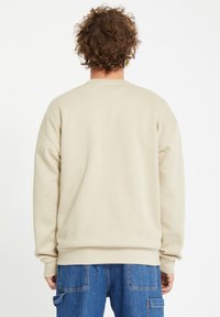 Beige crewneck sweatshirt with a relaxed fit, ribbed cuffs, and hem, worn with blue cargo jeans, showcasing a soft, smooth texture.