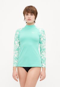 Long-sleeve turquoise rash guard featuring solid body and white floral patterned sleeves; smooth texture; front logo detail in white.