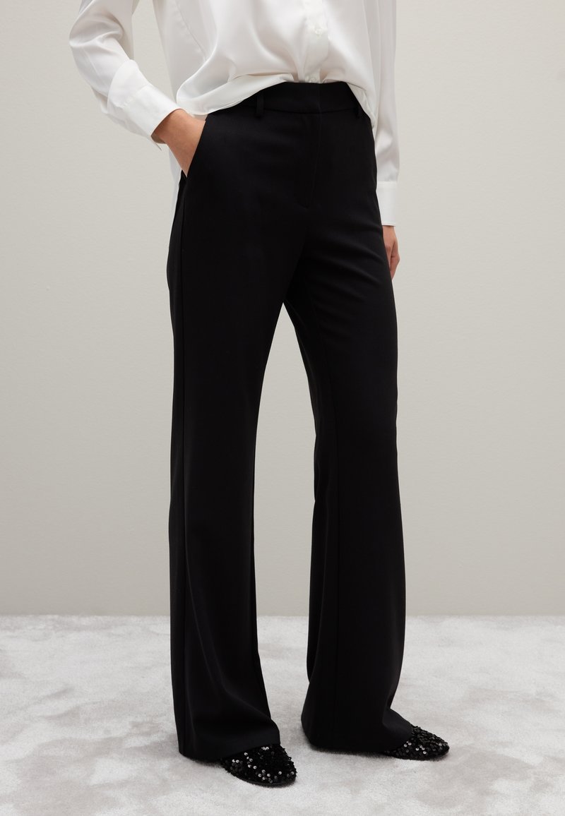 Pantaloni neri su misura con un design a gamba dritta, realizzati in tessuto liscio. Abbinati a scarpe nere con un accento di perline.