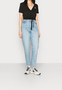 Czarna bluzka z krótkim rękawem, jasnoniebieskie jeansy z wysokim stanem i szare sneakersy z czarnymi akcentami, na jednolitym tle.