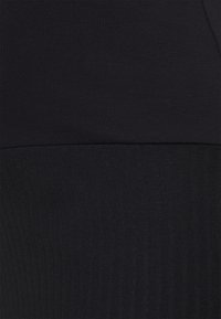Schwarzes Sportoberteil mit glatter, figurbetonter Oberseite und strukturiertem geripptem unteren Abschnitt. Nahtloses Design über das gesamte Oberteil.